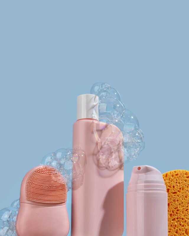 Pink tubes with cosmetics for skin and hair care stand on a glass shelf on light blue background. Moisturizing and cleansing concept. Set of accessories for hygiene. Natural organic spa cosmetic concept, minimalism brand packaging mock up.