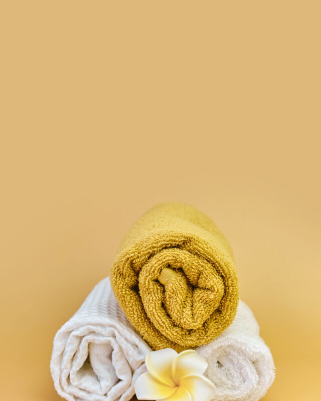 Stack of roll folded towels on a beige background, waiting to be used. Showcase of a cozy soft bathroom or spa setting. Studio shot, close up, copy space.